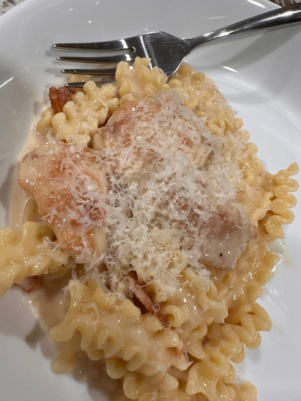 Chicken Marsala with pancetta on a white plate — browned chicken and crisped pancetta over ruffled ribbon pasta in a pale cream sauce, under a heavy shower of finely grated parmesan.