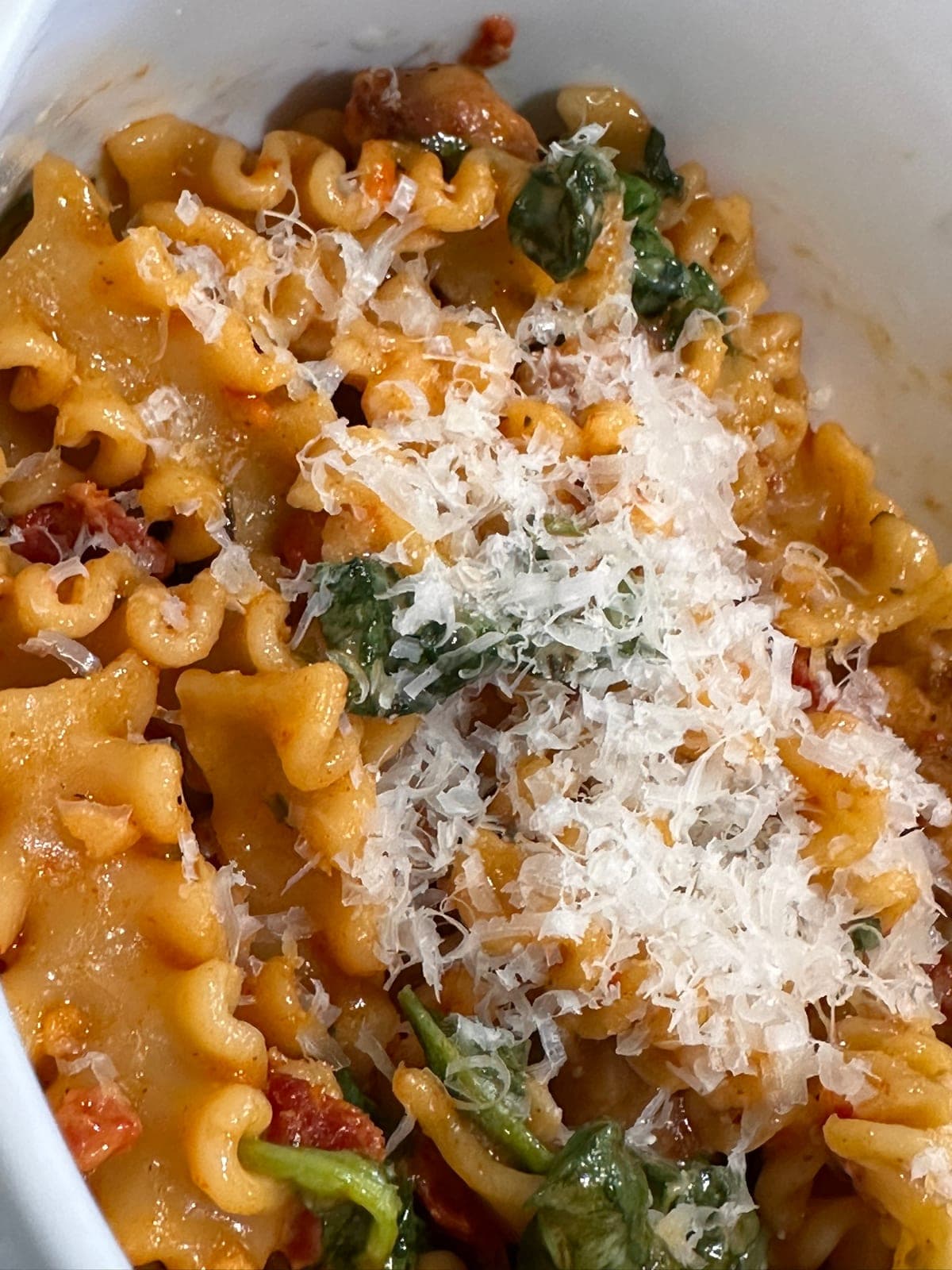 Marry Me Chicken Pasta in a white dish — ruffled ribbon pasta in a creamy sun-dried tomato sauce with wilted spinach, under a heavy shower of finely grated parmesan.
