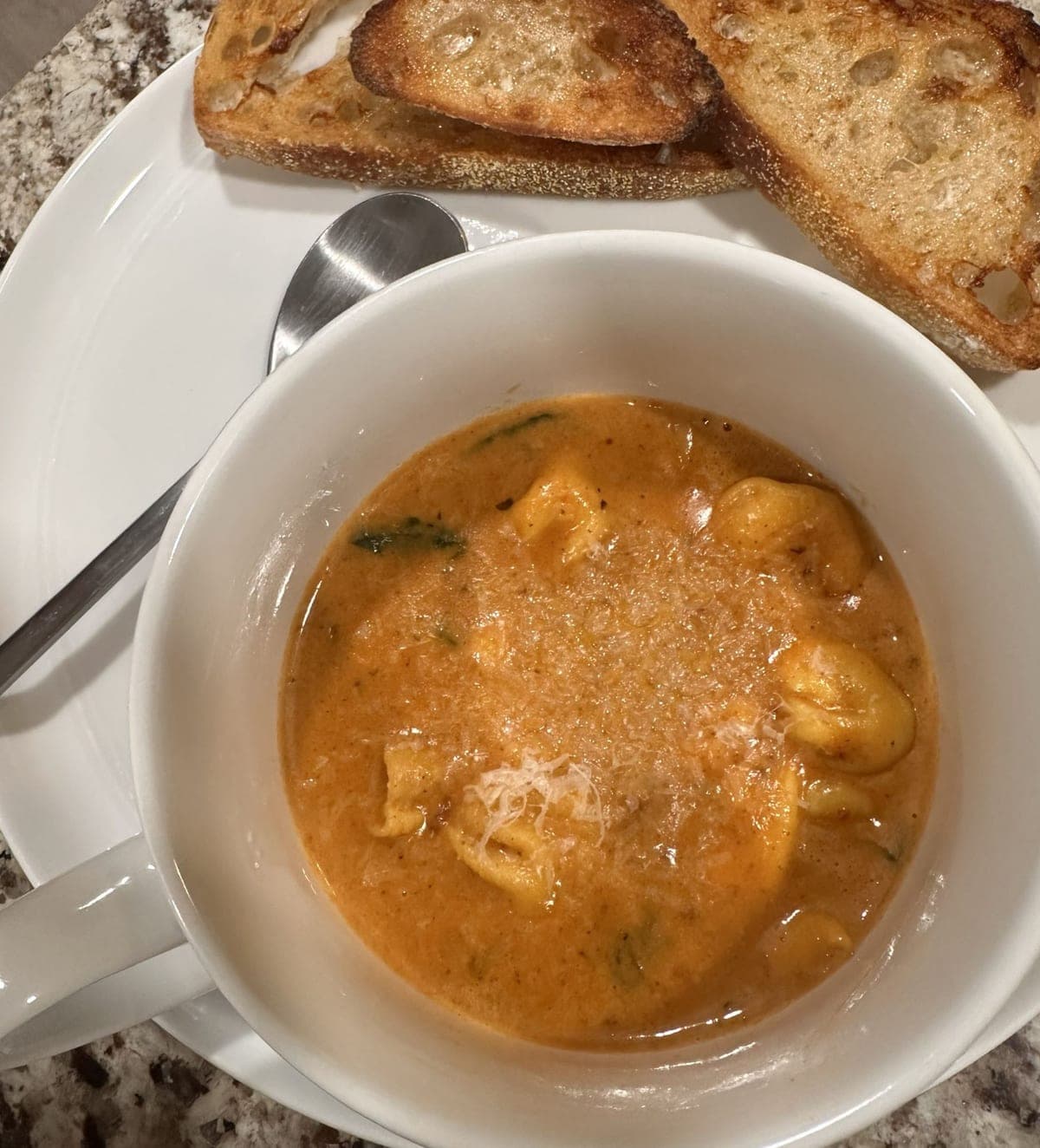 Sausage tortellini soup in a white bowl — cheese tortellini and wilted spinach in a creamy tomato broth under finely grated parmesan, with toasted baguette slices alongside.
